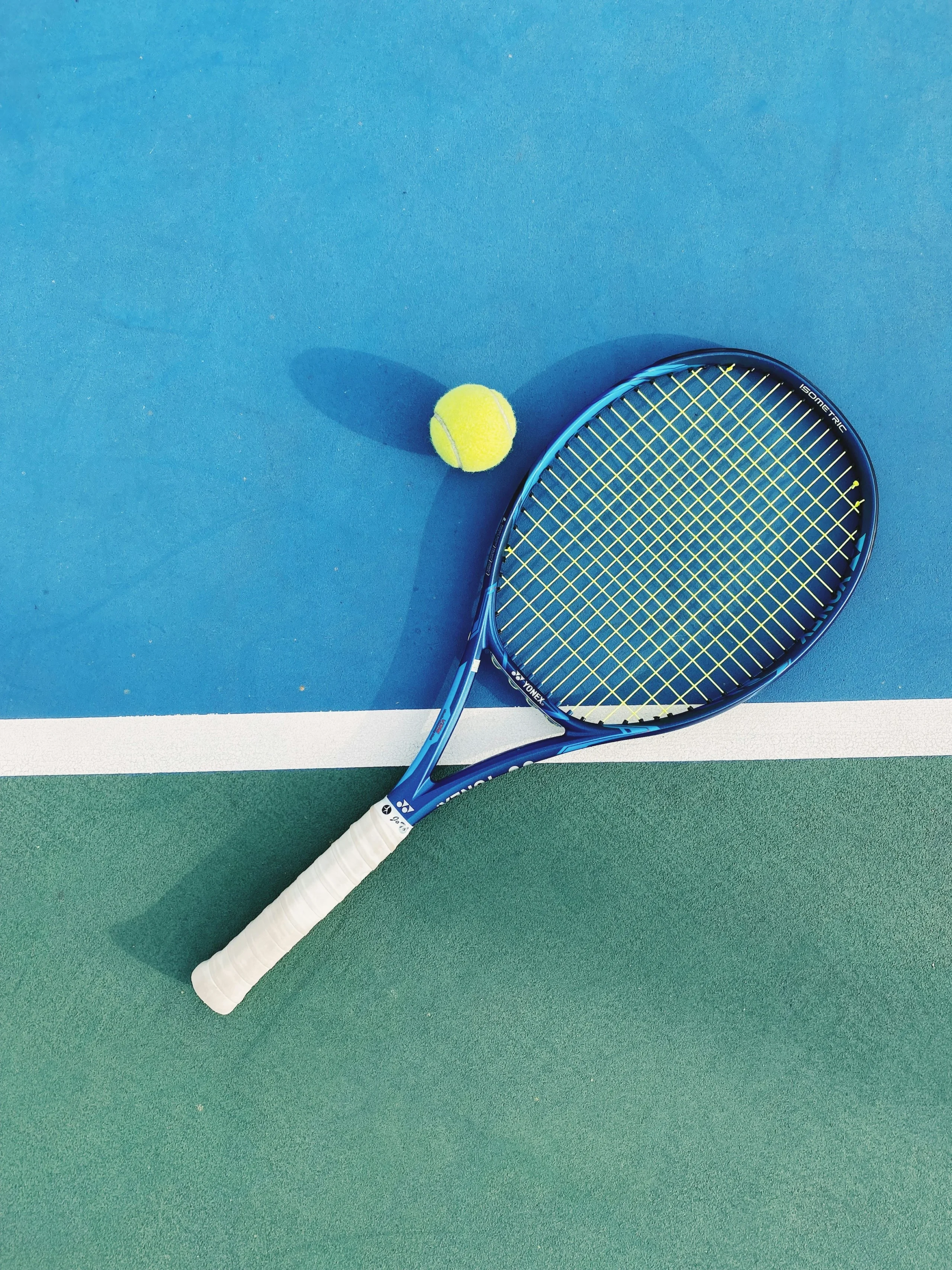 Raquette de tennis bleue et balle jaune sur un court vert et bleu, près de la ligne blanche. Raquette de tennis bleue et balle jaune sur un court vert et bleu, près de la ligne blanche.